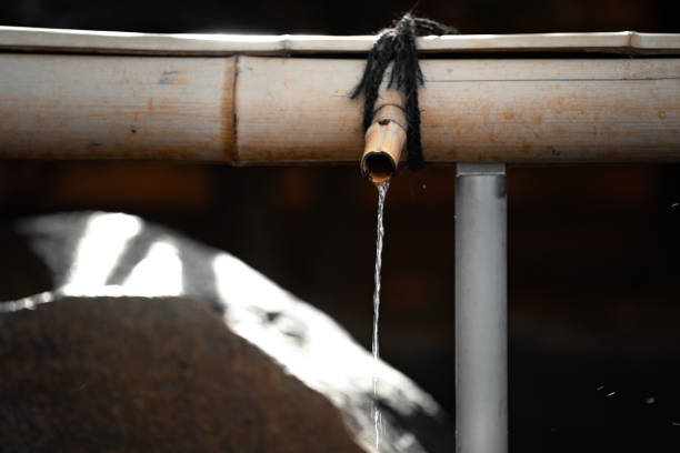 A bamboo water spout with clear water gently flowing from it, captured in a serene traditional setting. The focus is on the natural materials and calming flow of water, emphasizing tranquility and simplicity.