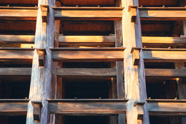 Close-up of a traditional wooden architectural structure, bathed in warm golden lighting. The intricate wooden beams and support highlights craftsmanship and structural design.