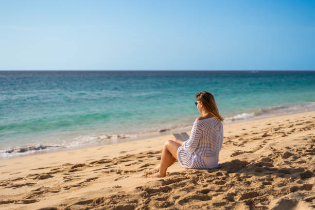 istock Woman relaxing on beach reading book 2153671089