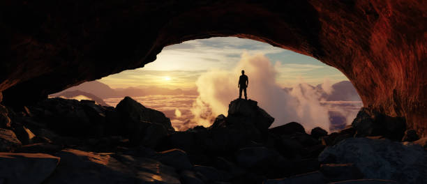 istock Adventure Man Standing in a Cave. Mountain Landscape in Background. Dramatic Sunset. 2153676605