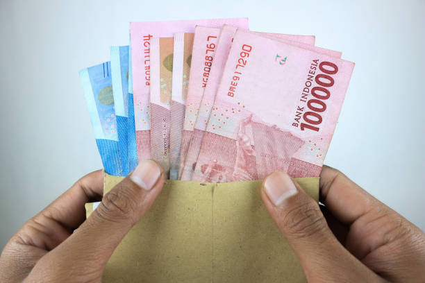 female hands holding open craft paper envelope with one hundred thousand rupiah banknotes