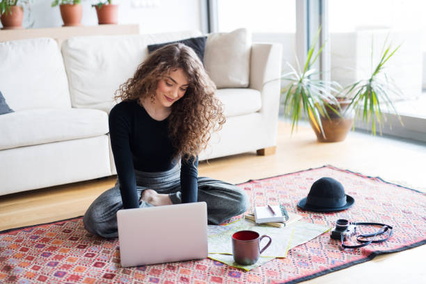 istock Beautiful woman planning summer vacation abroad, going on trip alone. Sitting on floor, working on itinerary on laptop. 2153690121