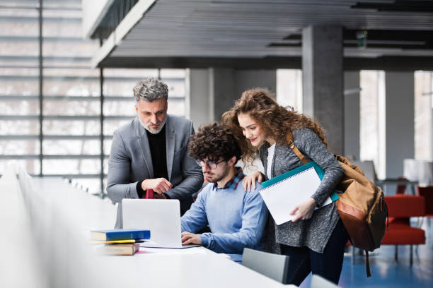 istock Handsome university professor helping to student final project, showing him research paper, book for thesis in library. 2153693024