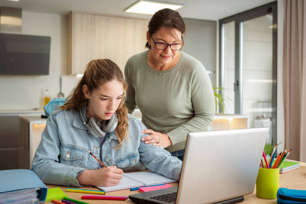 istock Schoolgirl and her mother doing homework at home. She is having online class using laptop 2153701602