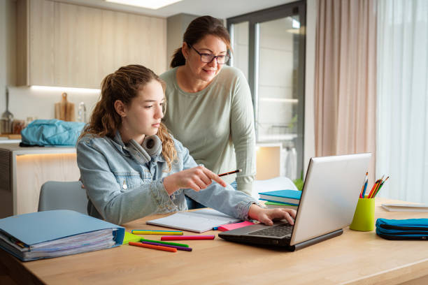 Schoolgirl doing homework with her mother. She is having online class using laptop