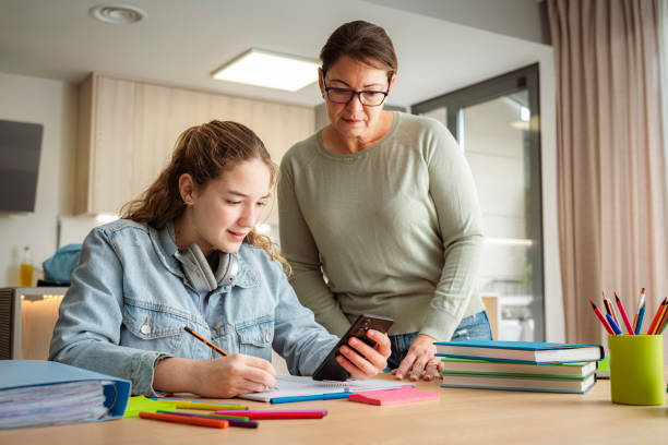istock Schoolgirl and her mother doing homework at home. She is using smartphone to get information 2153701633