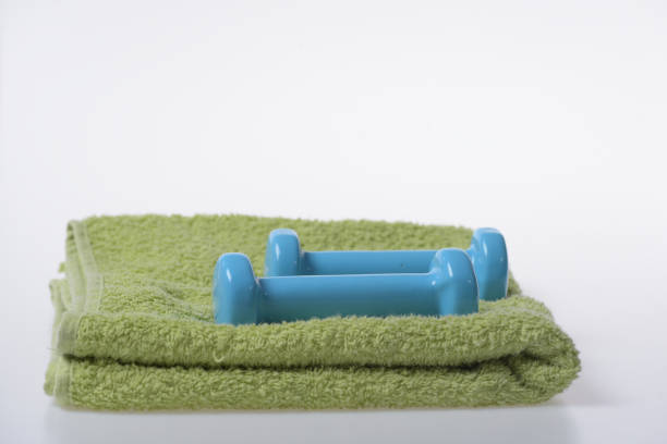 Dumbbells made of blue plastic on white background. Healthy lifestyle and sports concept. Barbells in small size on green soft towel, copy space. Health regime and fitness symbols.