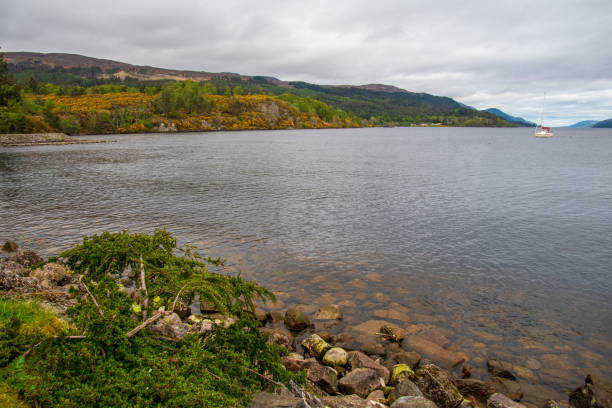 Water of Loch Ness in a cloudy day, boat visible in a distance, hills surrounded, picture was taken from a shore in Fort Augustus