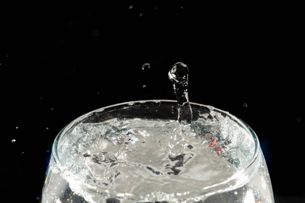 istock Close-up of a transparent glass cup with water inside and drops making a splash. 2153728983
