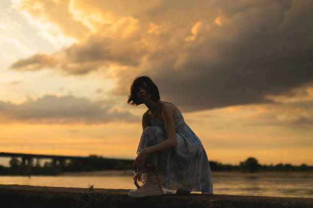 A woman gazes out over a river at sunset from the riverbank
