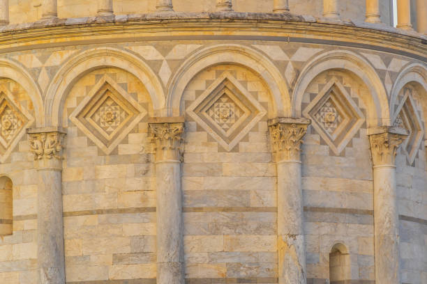Low angle view of the ornate facade of the Cattedrale di Santa Maria Assunta, featuring detailed carvings and statues. The Romanesque architectural style is highlighted by the intricate stonework and arches. The historic structure is located in Pisa, Italy.