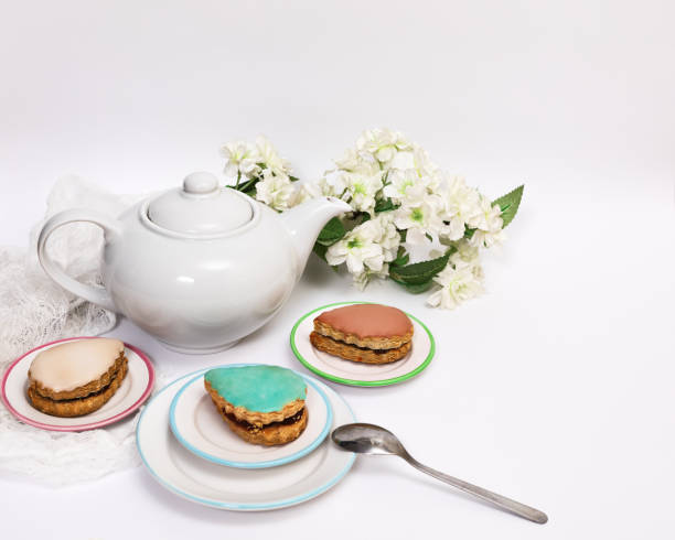 istock Multi-colored cake (turquoise, beige, pink, yellow and caramel) served on saucers around a white teapot on a white background with flowering branches 2153748162