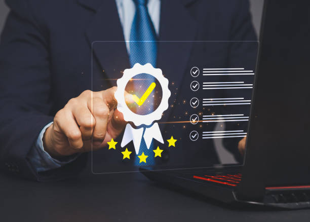 istock Businessman touches the quality symbol on an online document checklist on a virtual screen while sitting at a desk. 2153757838