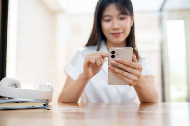 istock A beautiful, happy Asian woman using her smartphone while sitting in a cafe or co-working space. 2153760717