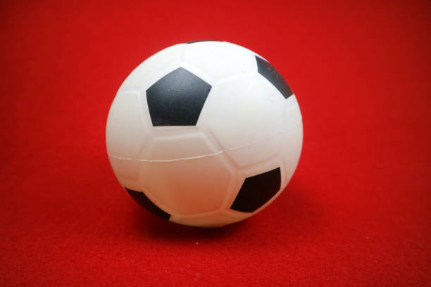 istock a small white and black toy rubber ball. Red background 2153764872