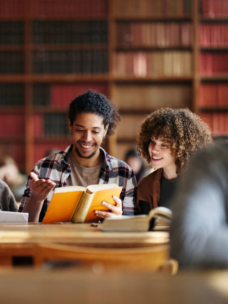 istock Happy university friends studying from book in library. 2153768697