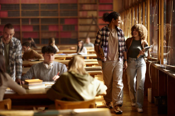 istock Happy college couple talking while walking through full library. 2153769853