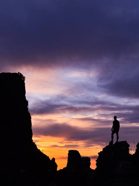 Silhouette of man standing on rocks on a mountain looking towards the dramatic sky, Table Mountain, Cape Town, South Africa