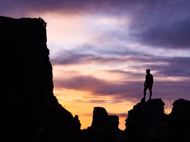 Silhouette of man standing on rocks on a mountain looking towards the dramatic sky, Table Mountain, Cape Town, South Africa