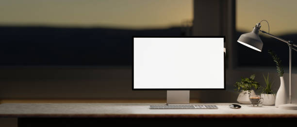 istock A computer desk in a modern, dark room in the evening features a white-screen computer mockup. 2153781032