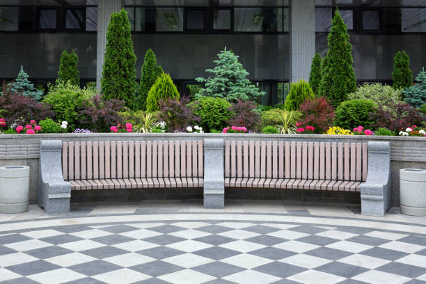 Large beautiful wooden bench with stone railings. Against a background of flowers and green ornamental shrubs.