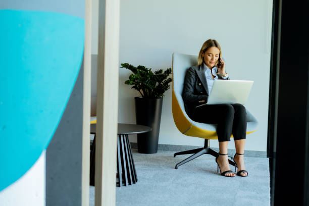 istock Businesswoman in modern office talking on phone and using laptop during daytime 2153787748