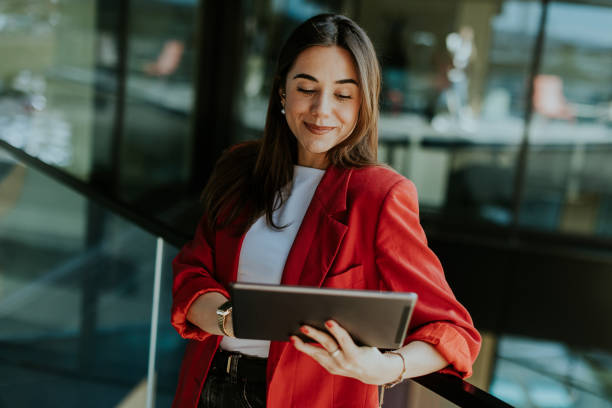 istock Smiling businesswoman in red blazer using tablet at modern office window in daylight 2153788243