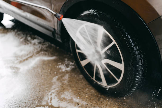 A mature man cleaning his car at a self-service car wash, using water, soap, and a sponge for a thorough wash