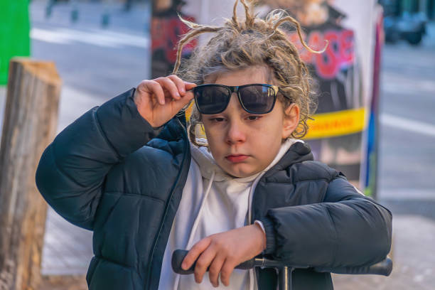 boy with dreadlocks and sunglasses with his scooter in the city. The look of him with freedom and style. The urban background highlights his bold presence, capturing a moment of youthful adventure and urban exploration.