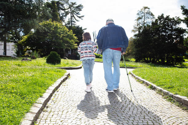 Elderly couple walking in the park. Senior man is blind and senior woman helping him to walk. Senior couple spending time in nature. Senior couple enjoying outdoors retirement.