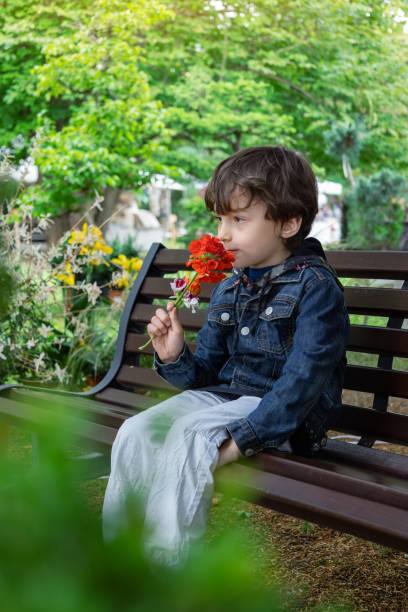 istock Child sitting on bench with flowers in hand 2153801338