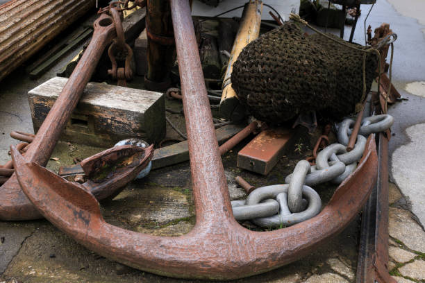 A rusty anchor hangs on the bow of a black sailboat. A draft scale is on board the vessel.