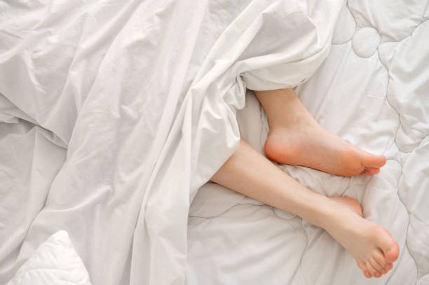 istock Bare feet in bed under white cotton blanket, good sleep, comfort sleeping bedding concept, minimalist Nordic bedroom 2153806957