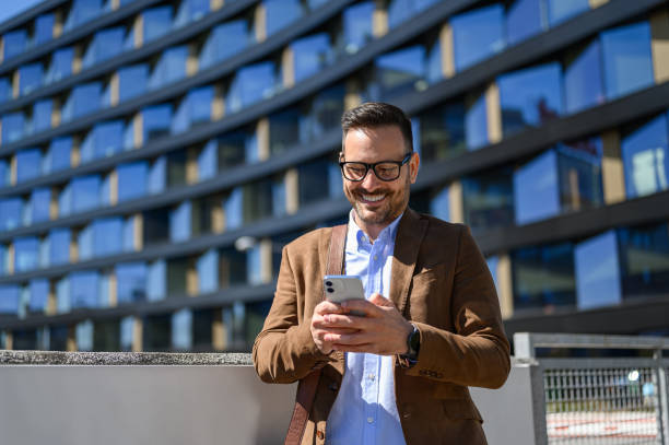 istock Male professional smiling and texting over smartphone while standing against modern building in city 2153810307