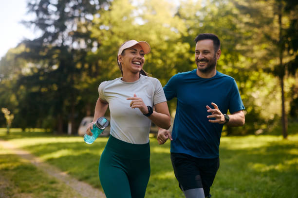 Cheerful athletic couple jogging through the park. Happy athletic couple having fun while running together in nature. Copy space. adults exercising stock pictures, royalty-free photos & images