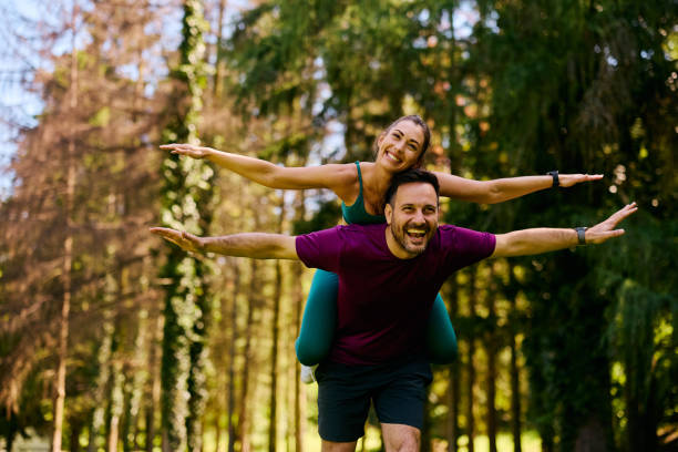 istock Playful athletic couple having fun while piggybacking with arms outstretched in nature. 2153824042