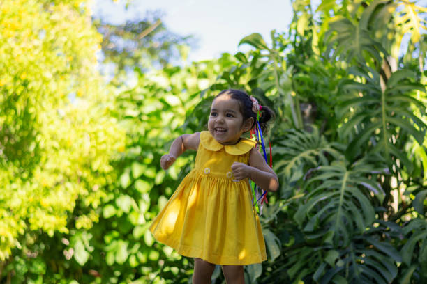 Portrait of a happy little girl playing in the natural yard in her yellow dress.