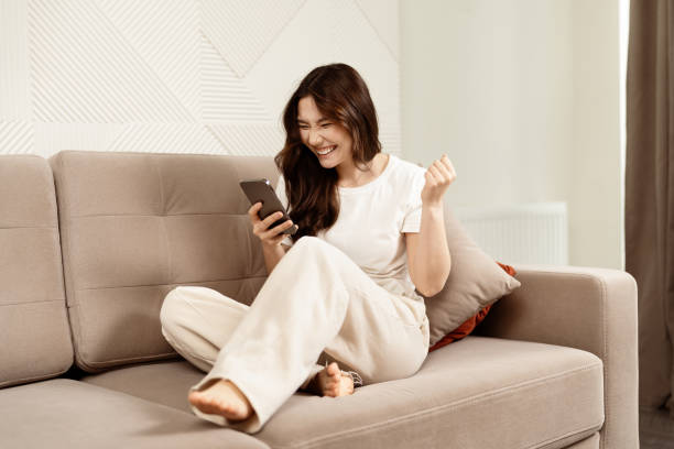 istock Happy Young Woman On Sofa Winning On Smartphone App 2153835496