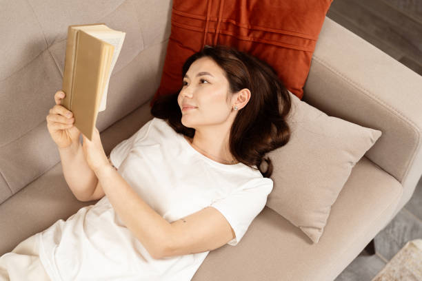 istock Young Woman Relaxing on Couch Reading a Novel at Home 2153835542