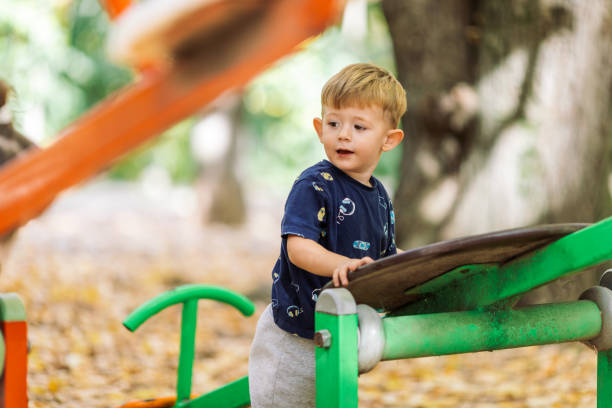 A young boy playfully hangs upside down on yellow playground equipment. He is wearing a green shirt and appears to be having fun in a park setting.