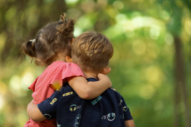 Two toddlers, a boy and a girl, brother and sister, walking and hugging in the city park. They look happy.