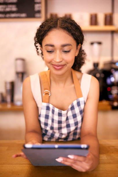 istock Young Woman Using Digital Tablet Wearing Apron Working Behind Counter In Coffee Shop Or Cafe 2153841018