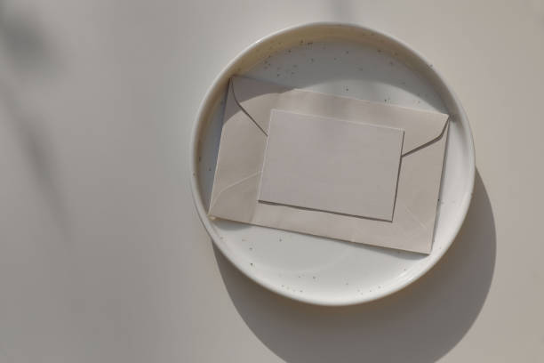 istock Blank business card, invitation mockup, envelope in sunlight. Spotted ceramic plate on beige table background. Soft shadows. Neutral wedding stationery. Food, restaurant, craft concept, flat lay. Top. 2153841583