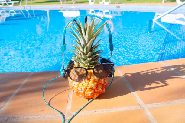 pinapple near swimming pool in sunglasses and headphones