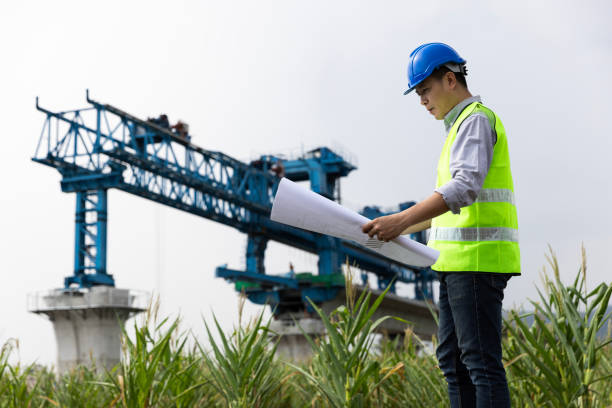 Civil engineer or construction engineer with green safety vest and blue hardhat hold blueprint drawing work , infrastructure