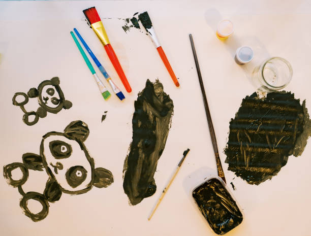 istock Two panda bears painted on a white sheet next to brushes and jars of paint 2153855856