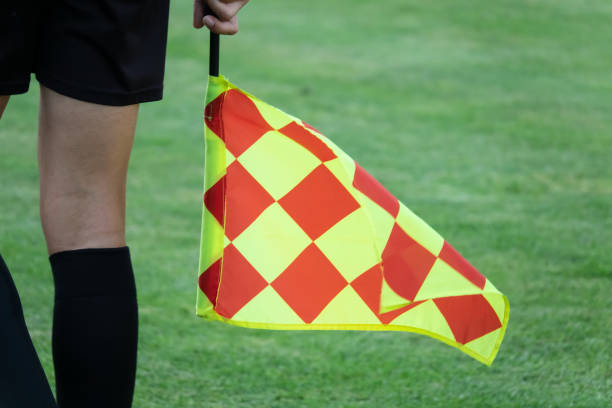 Referee holds up red card during football match, players arguing with referee.