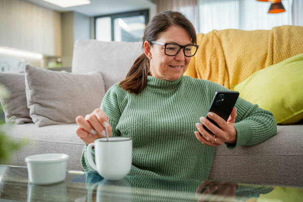 istock Distracted woman using phone while drinking coffee or tea in living room 2153864493