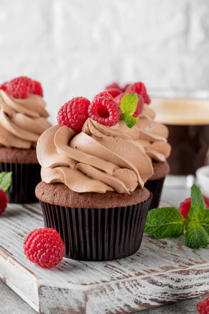istock Chocolate cupcakes with cream decorated with fresh raspberries and mint leaves on a gray concrete background. Delicious holiday dessert 2153866762