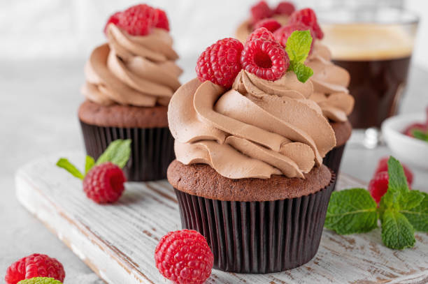 istock Chocolate cupcakes with cream decorated with fresh raspberries and mint leaves on a gray concrete background. Delicious holiday dessert 2153866764